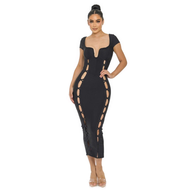 Load image into Gallery viewer, A model poses in a black Bandage Midi Slit Bodycon Dress featuring a unique wired neckline and faux lace-up details along the sides, styled with transparent heels.
