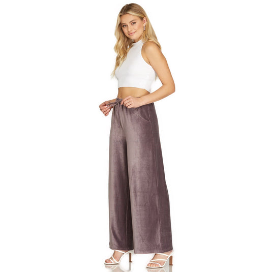 Model turned slightly, giving a three-quarter view of the velvet wide-leg pants in mauve with elastic waistband and pockets, complemented by a white crop top.