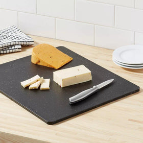 A black polygranite cutting board on a kitchen counter, adorned with sliced cheese and a knife, showcasing practicality and style.