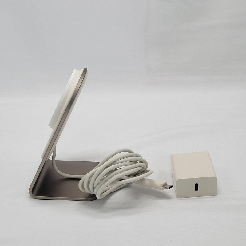Load image into Gallery viewer, Side view of a wireless charging stand showing the thin profile of the MagSafe compatible charging disk and its metallic base, with a coiled white USB-C cable and power adapter.
