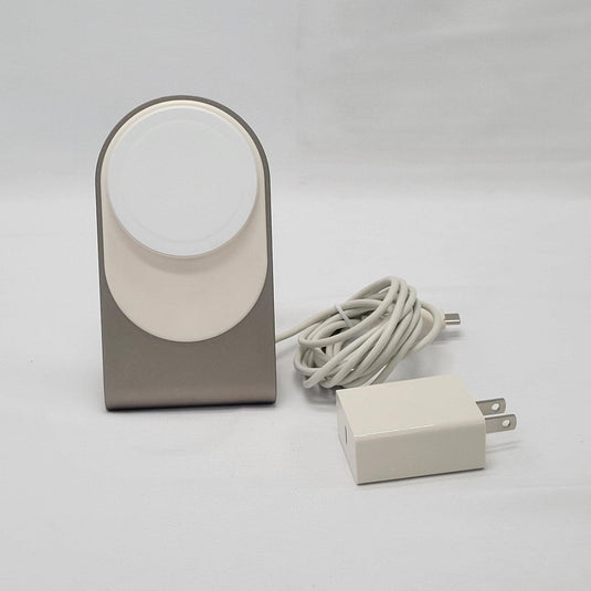 Elegant wireless charging stand with a MagSafe compatible charging disk mounted on a sleek metallic base, accompanied by a white USB-C cable and matching wall adapter on a white background.