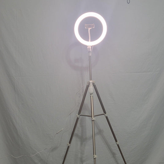 A luminous 10-inch Heyday ring light on a tripod, central phone clip empty, casting a soft light in a dimly lit room.