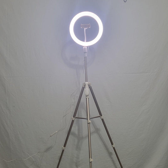 Front view of a 10-inch Heyday ring light mounted on a tripod, illuminated against a grey backdrop, with a power cable trailing to the side.