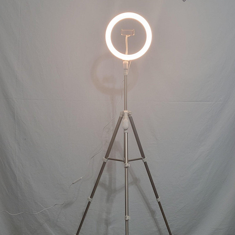 Load image into Gallery viewer, 10-inch Heyday ring light with a central phone holder, glowing warmly on a fully extended tripod against a plain background.
